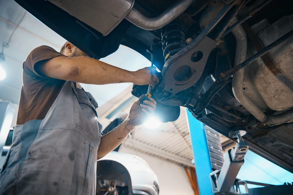 Mécanicien automobile travaillant sous un véhicule surélevé dans un garage professionnel, effectuant des réparations avec outillage spécialisé